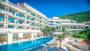 A hotel with a swimming pool, multiple balconies, and a mountainous backdrop. - Monte Casa Spa & Wellness (Petrovac)