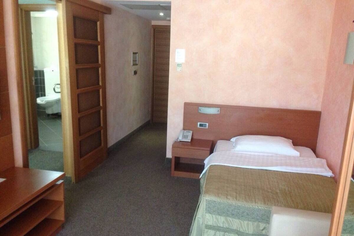 A hotel room with a bed, bedside table, and a wooden wardrobe.