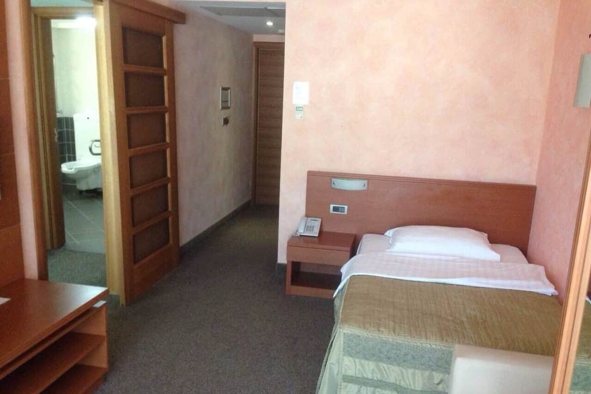A hotel room with a bed, bedside table, and a wooden wardrobe.