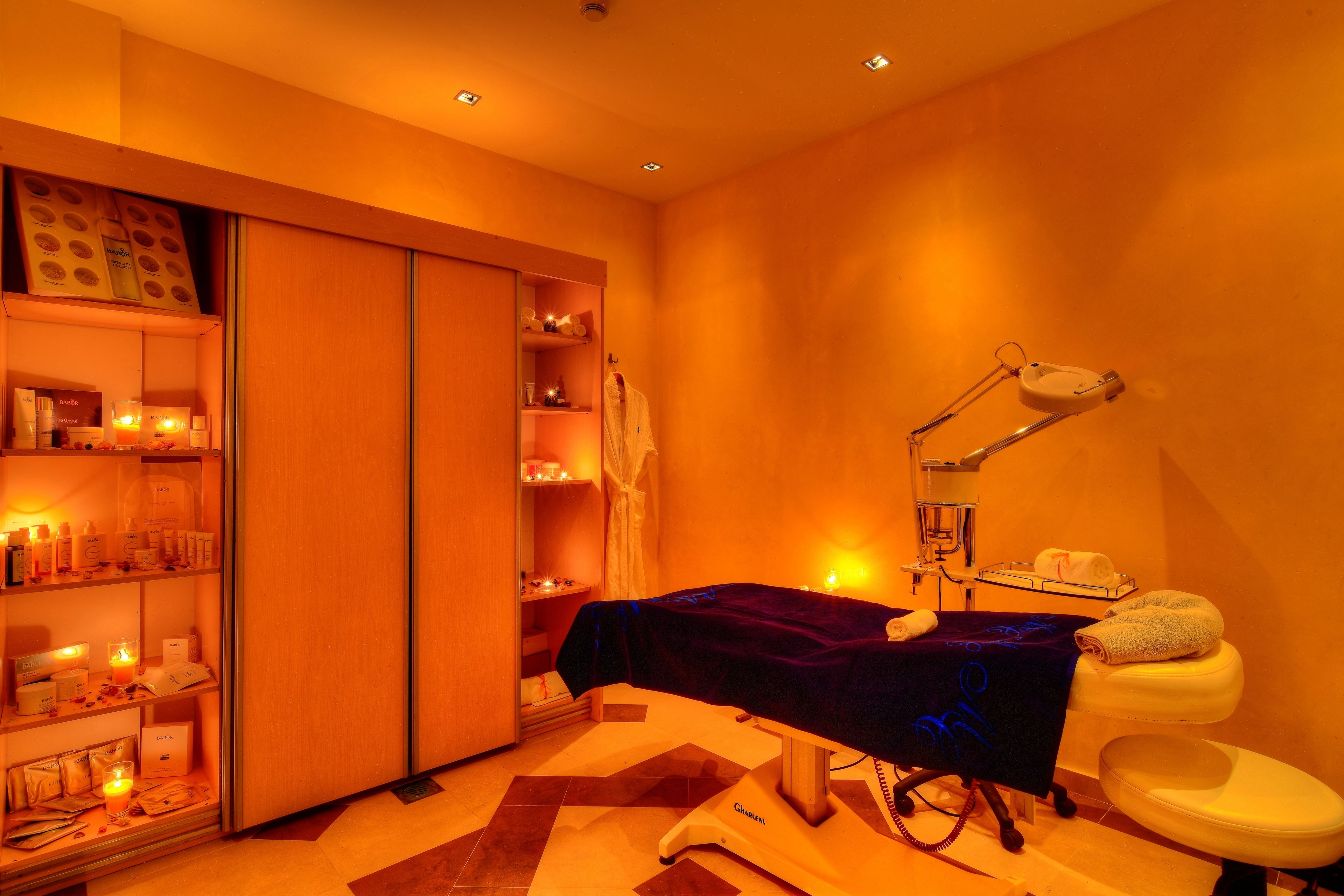 A room with a massage table, a toilet, shelves with toiletries, and a mirror.