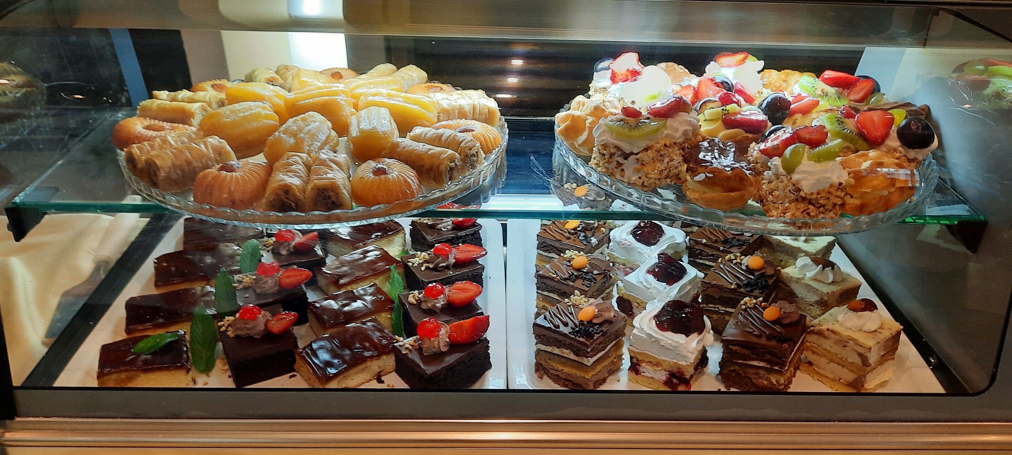 A display case with various pastries and desserts, including croissants, fruit-topped cakes, and chocolate desserts.