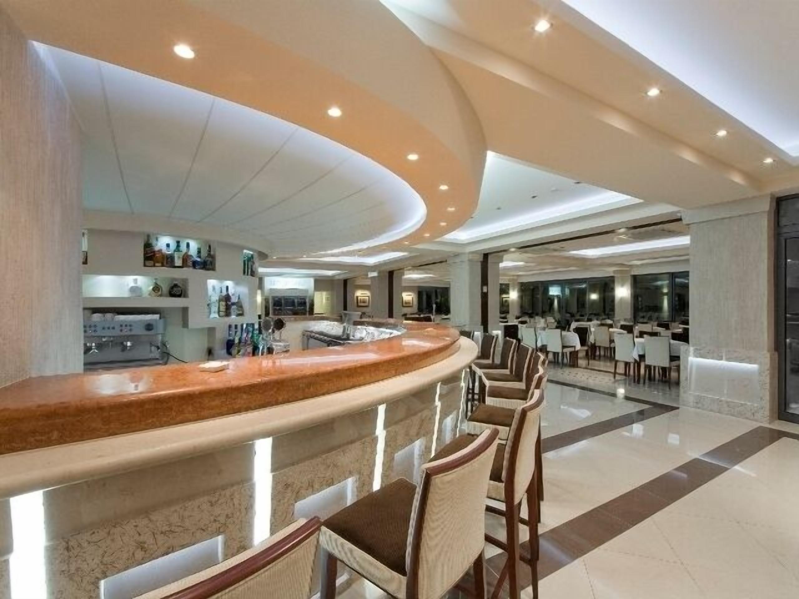 A modern hotel lobby with a curved reception desk, seating area, and a dining section.