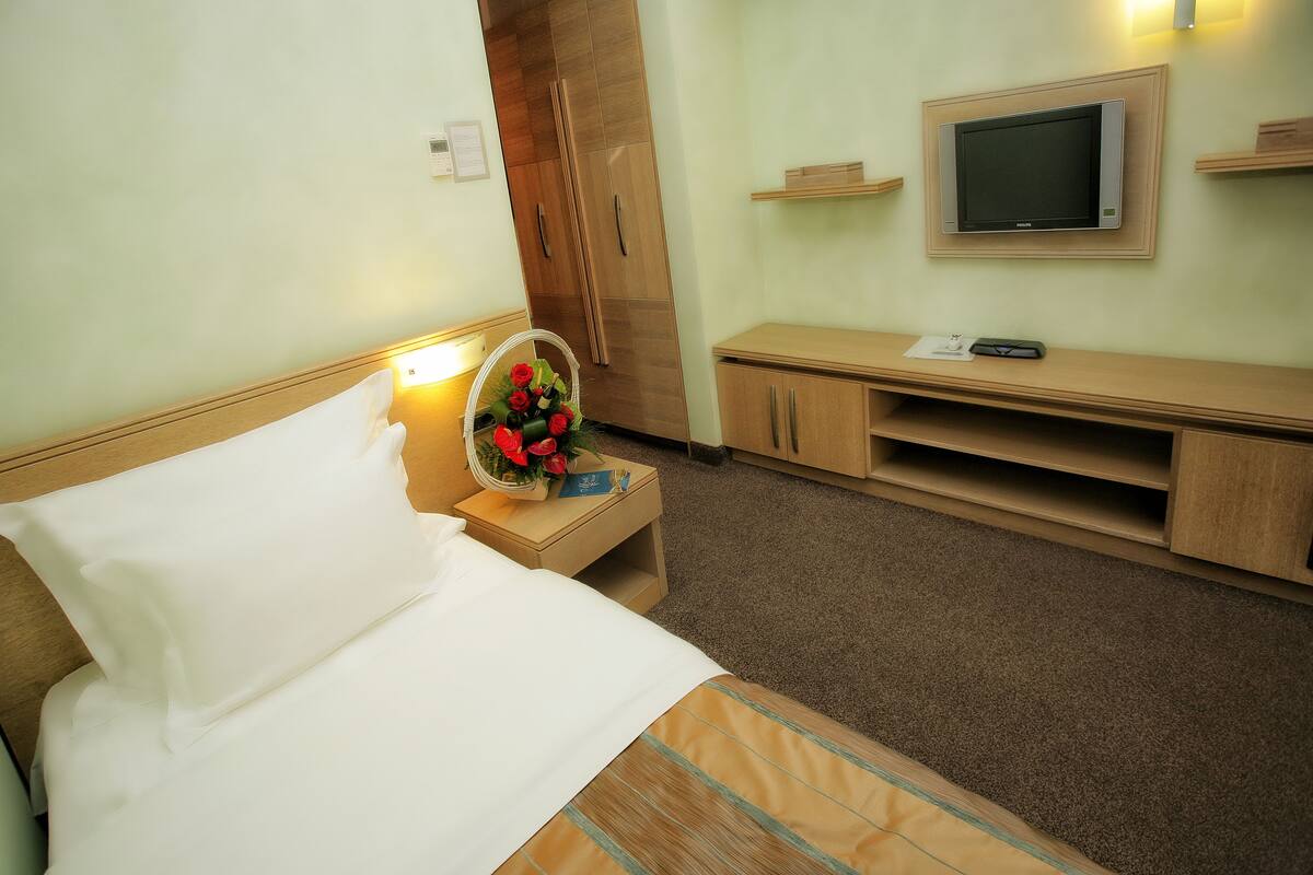 A hotel room with a bed, bedside table with a lamp, a TV mounted on the wall, and wooden furniture.