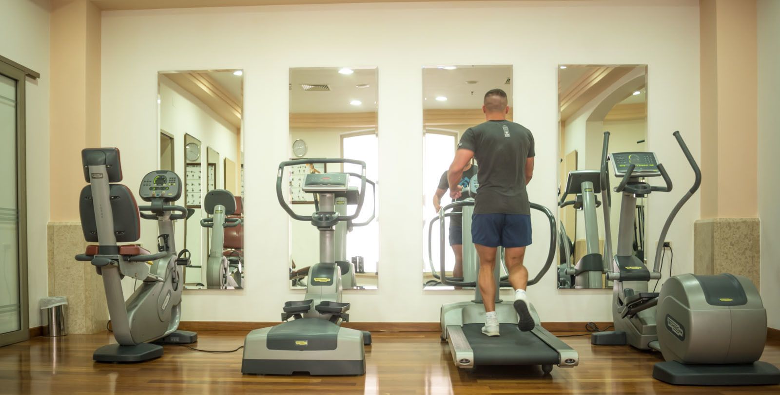 Une salle de sport équipée de divers appareils d’exercice, d’un tapis de course et d’un miroir qui reflète l’ensemble de la pièce.
