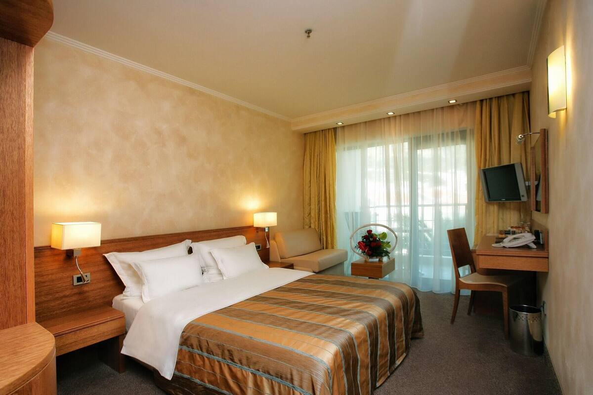 A hotel room with a large bed, a desk with a chair, a television, and a desk lamp.