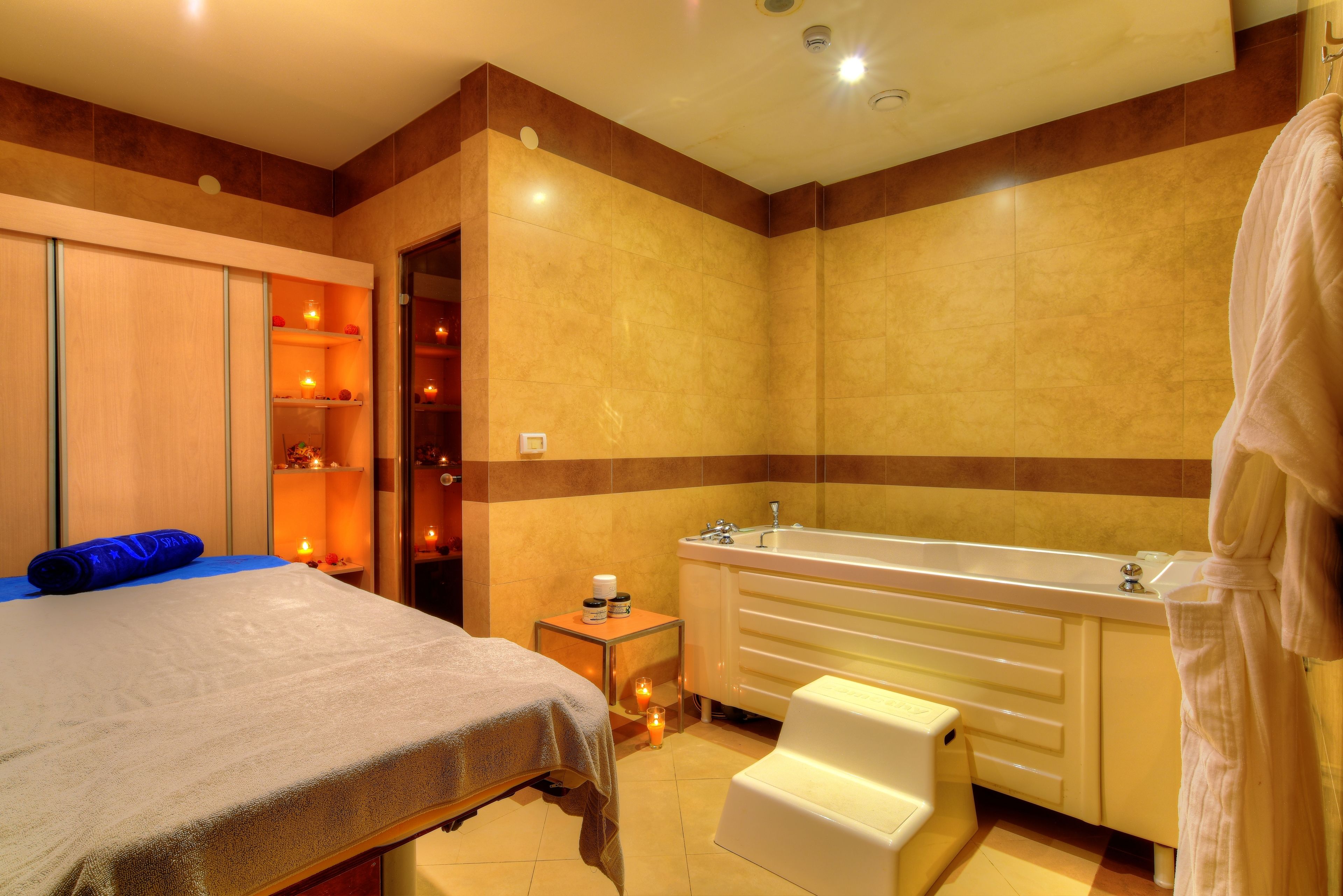 A hotel bathroom with a large bathtub, a separate shower area, and a bed with a blue towel.