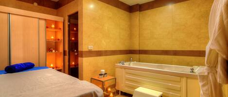 A hotel bathroom with a large bathtub, a separate shower area, and a bed with a blue towel.