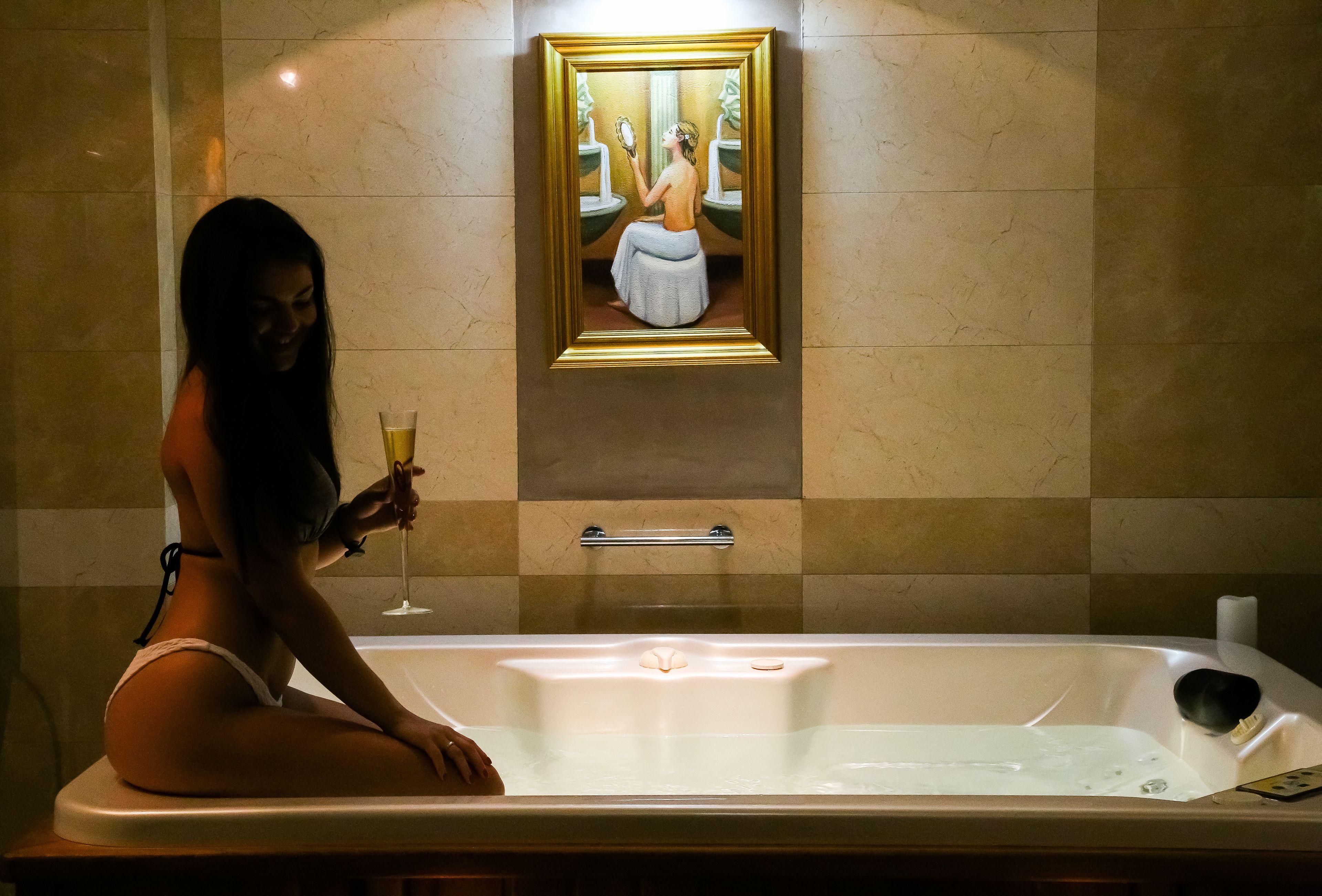 A person sitting in a bathtub with a framed artwork above them.