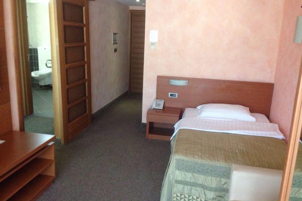 A hotel room with a bed, bedside table, and a wooden wardrobe.