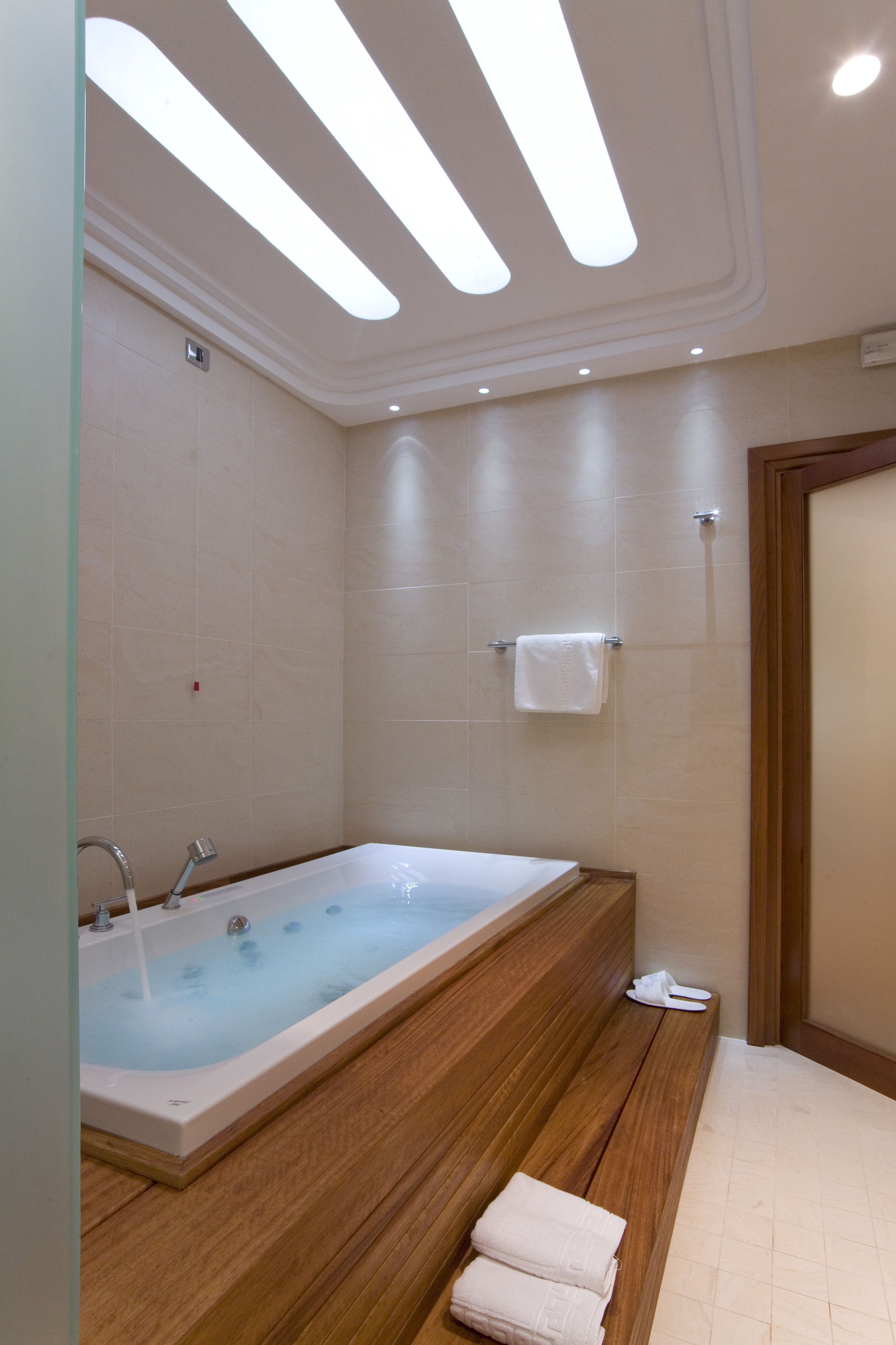 A modern bathroom with a large bathtub, wooden bench, and a towel rack.