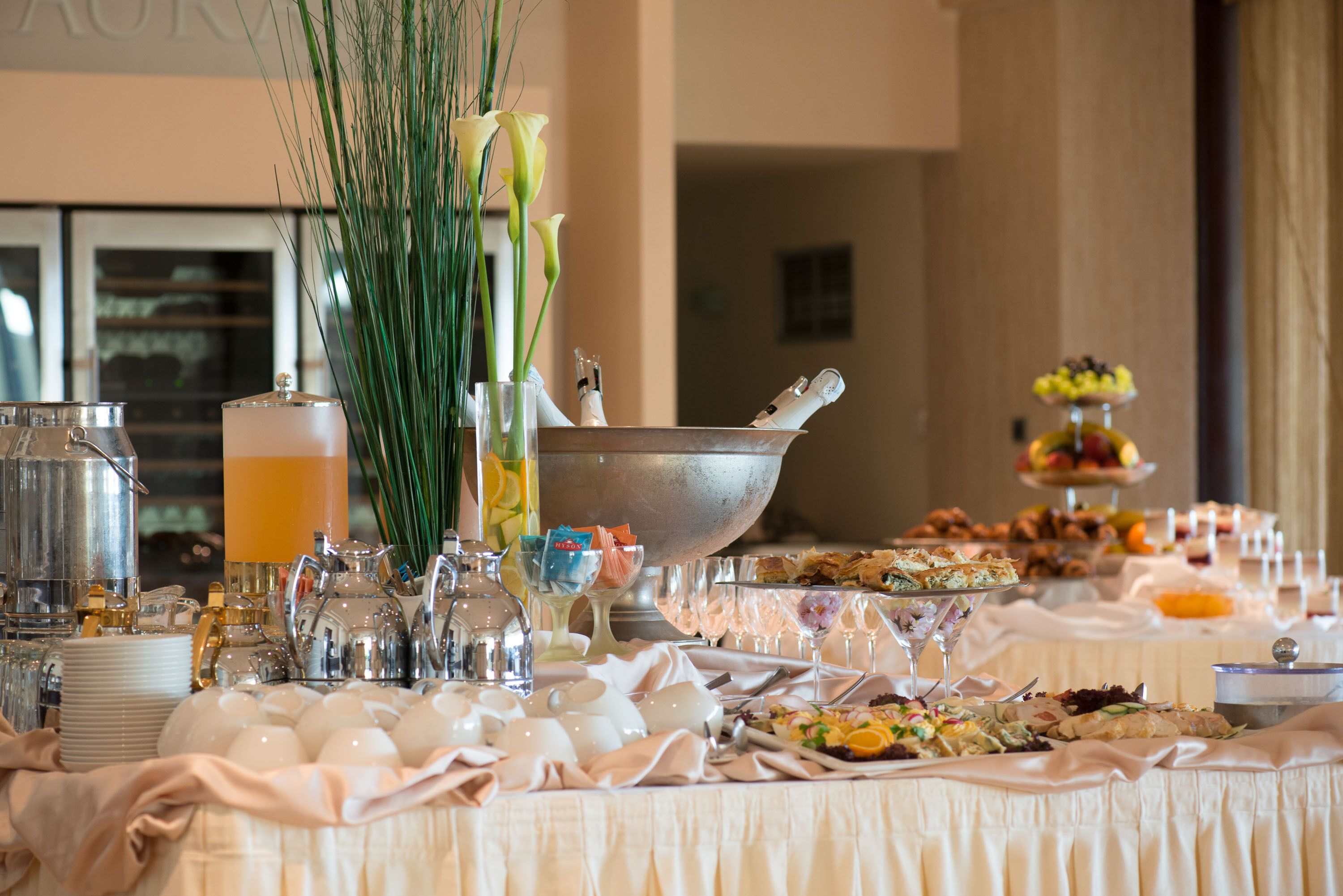Una mesa de buffet con diversos alimentos, un bol grande de metal y varios objetos de vidrio.