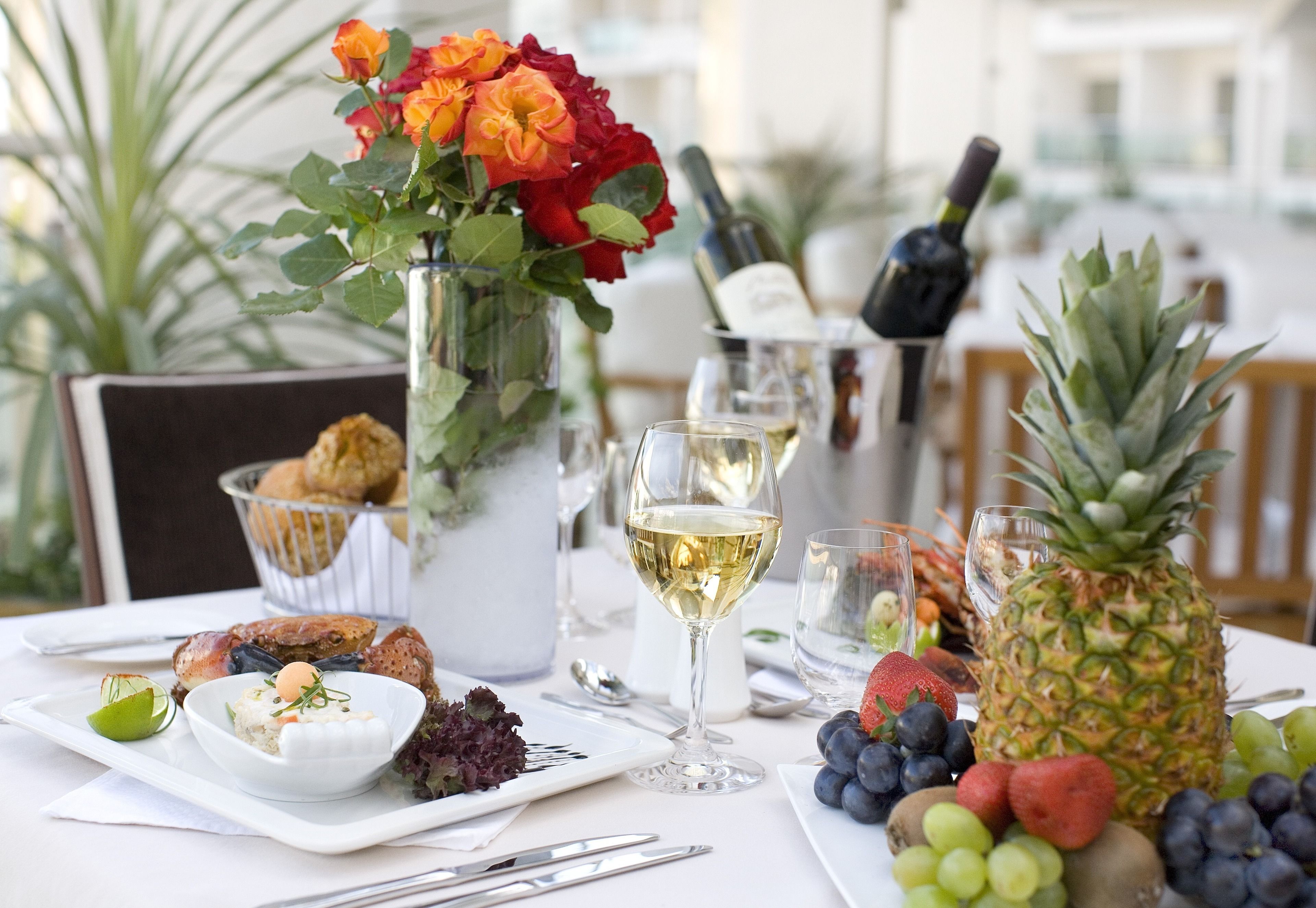 A table set with a variety of food items, including fruits, a bottle of wine, and a vase with flowers.