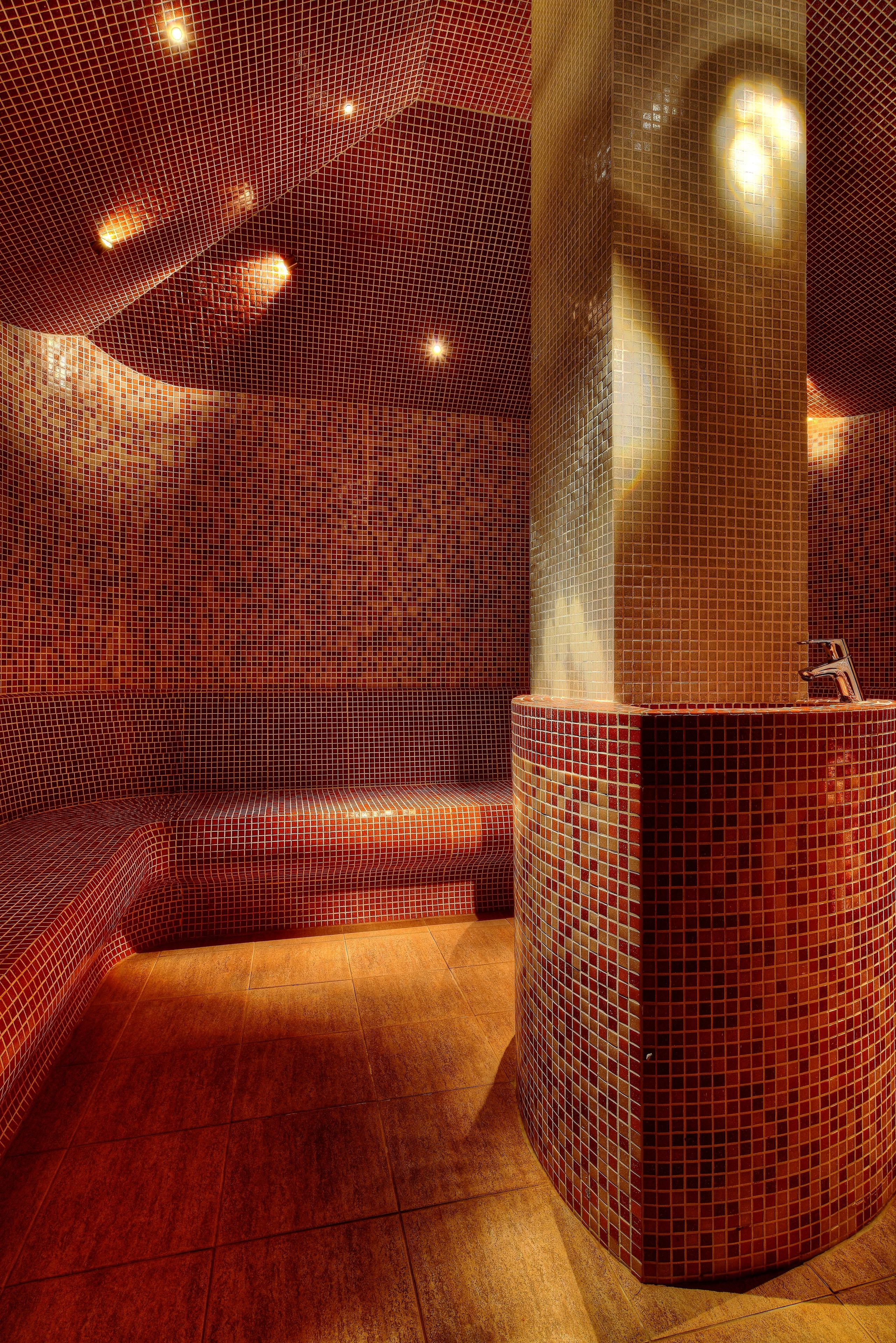 A modern bathroom with a mosaic tiled wall, a curved bench, and a central column.