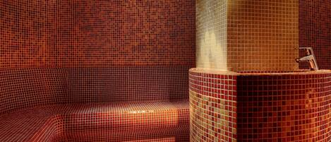 A modern bathroom with a mosaic tiled wall, a curved bench, and a central column.