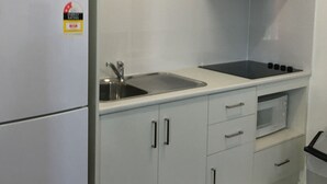 A kitchen with a refrigerator, sink, stove, microwave, and cabinets. - Footscray Motor Inn (Footscray)