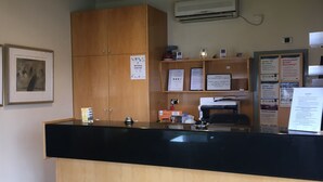 A reception desk with a black counter, wooden cabinets, and a mounted air conditioner. - Footscray Motor Inn (Footscray)