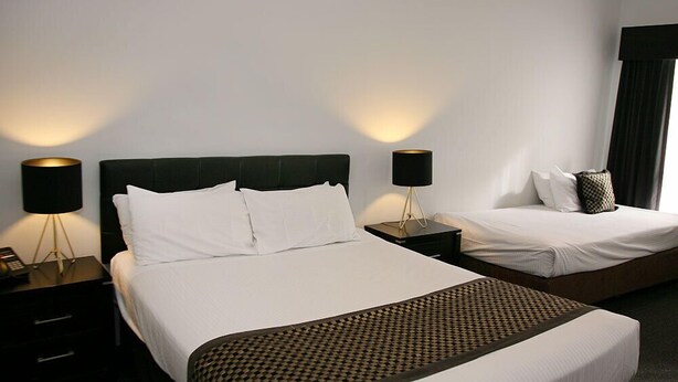 A hotel room with a large bed, two bedside tables, and two lamps. - Footscray Motor Inn (Footscray)
