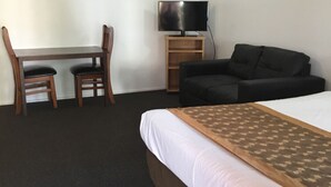 A hotel room with a bed, a desk with two chairs, a television, and a sofa. - Footscray Motor Inn (Footscray)