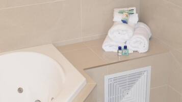 A bathroom with a white bathtub, beige tiled walls, and a towel rack with neatly folded towels and toiletries.