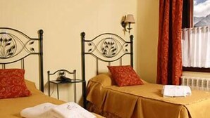 A room with two beds, each with a red pillow and a white towel. There is a small table with a lamp between the beds. - Campanilla (Ushuaia)