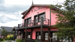 A pink building with a balcony, surrounded by a garden with various plants and flowers. - Campanilla (Ushuaia)