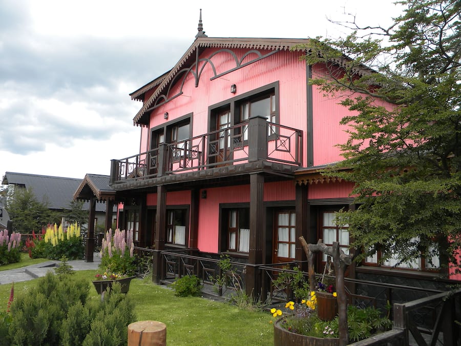 Ein pinkfarbenes Gebäude mit Balkon, umgeben von einem Garten mit verschiedenen Pflanzen und Blumen.