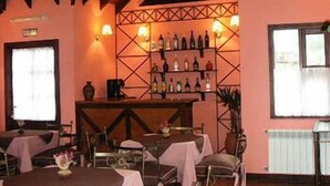 A restaurant with wooden beams, pink walls, and a bar area with bottles. Tables are set with white tablecloths and chairs. - Campanilla (Ushuaia)