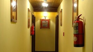A narrow hallway with yellow walls, a fire extinguisher mounted on the wall, and a framed picture on the wall. - Campanilla (Ushuaia)