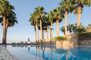 Zona de piscina con palmeras, sillas de descanso y un muro de piedra.