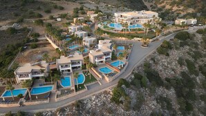 An aerial view of a resort with multiple buildings, swimming pools, and palm trees. - The Noverian Scenic Crete 5 Star Hilltop Villa Resort & Spa (Hersonissos)