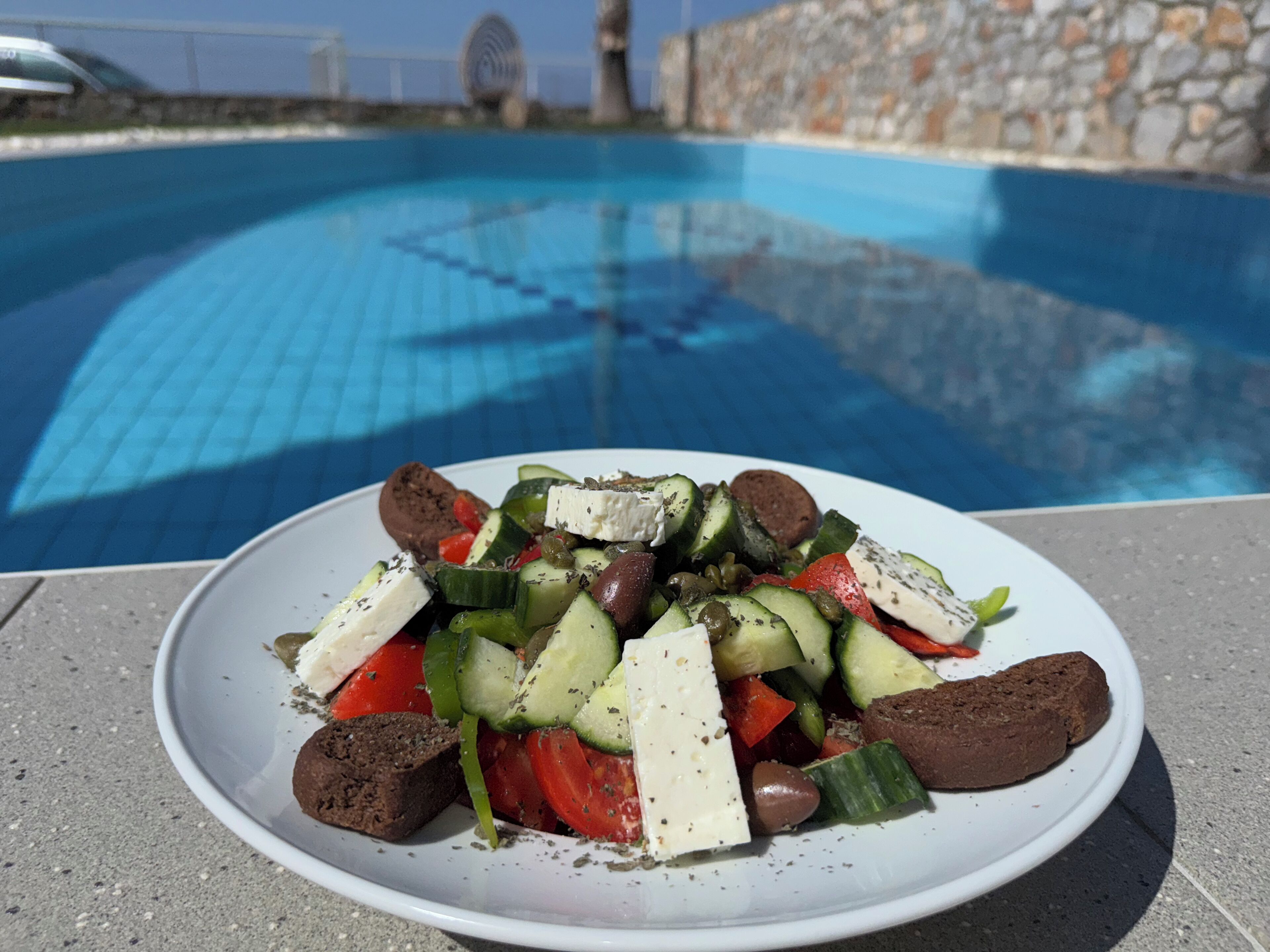A plate of food with vegetables and cheese by a poolside.