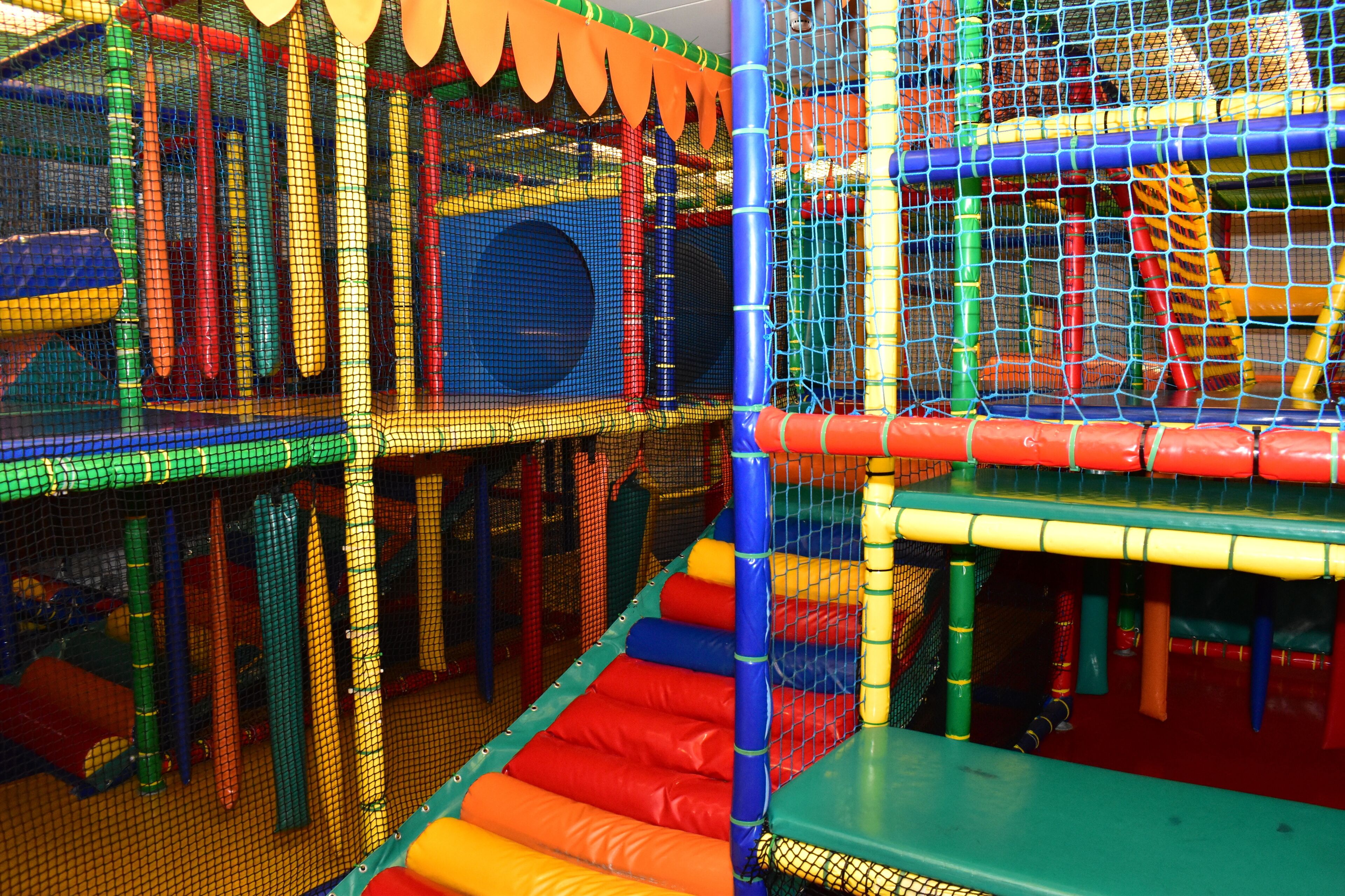 A multi-level indoor play area with netted structures and padded surfaces.