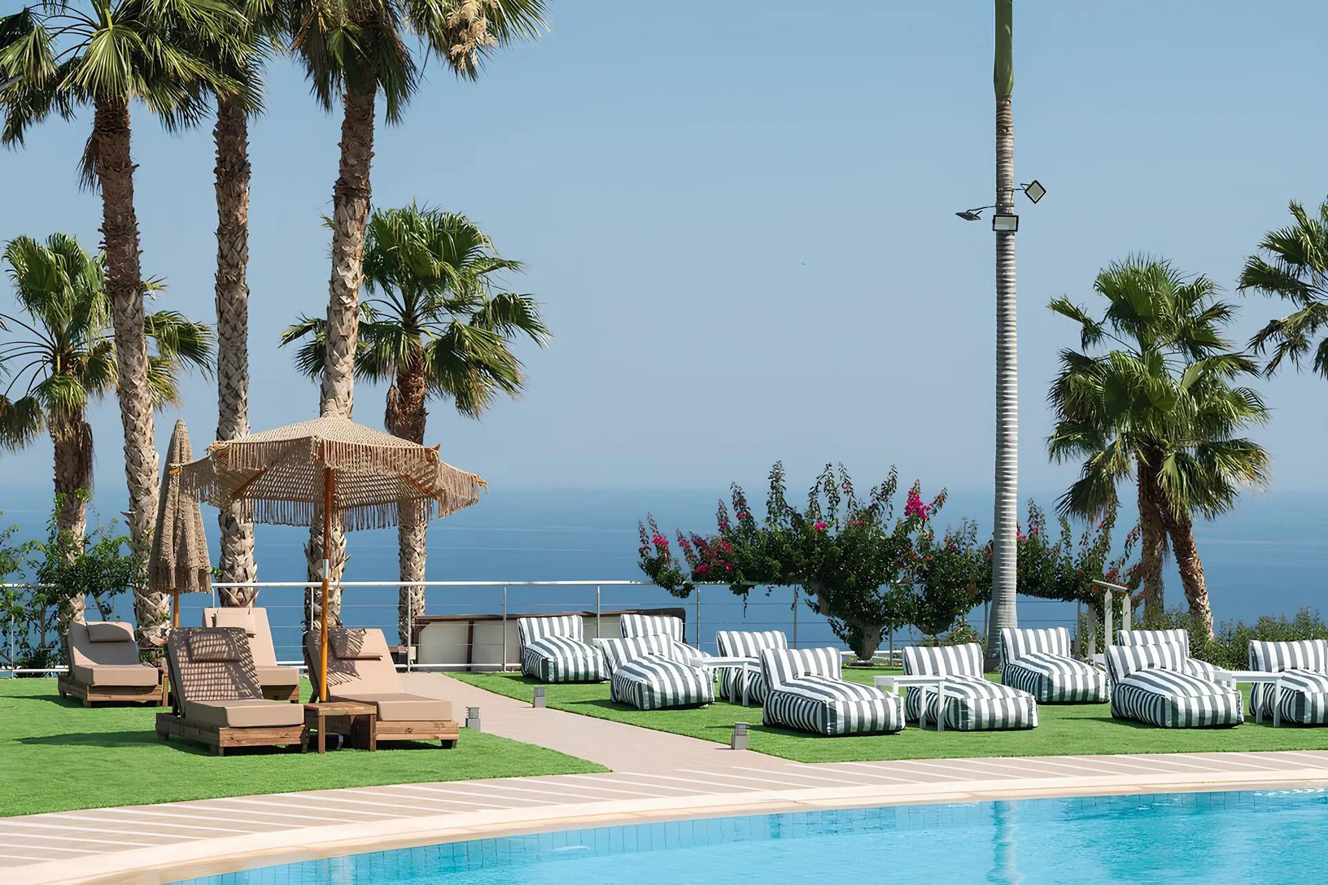 A poolside area with lounge chairs, a small hut, and palm trees.