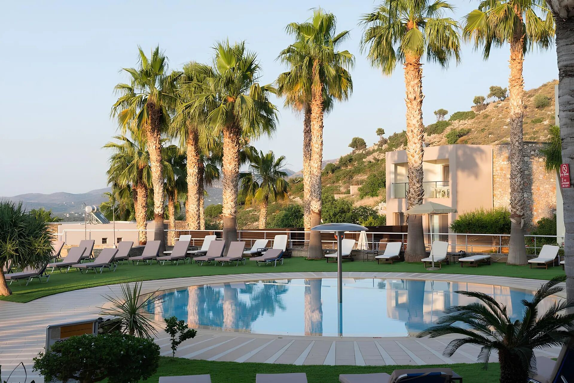 A poolside area with lounge chairs, palm trees, and a modern building in the background.