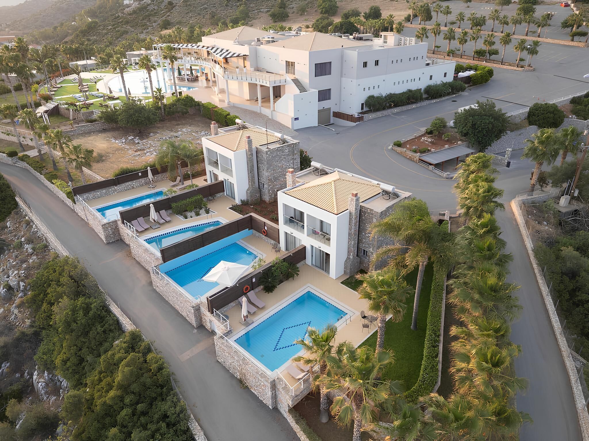 A modern resort with multiple swimming pools, a parking area, and a view of the surrounding landscape.