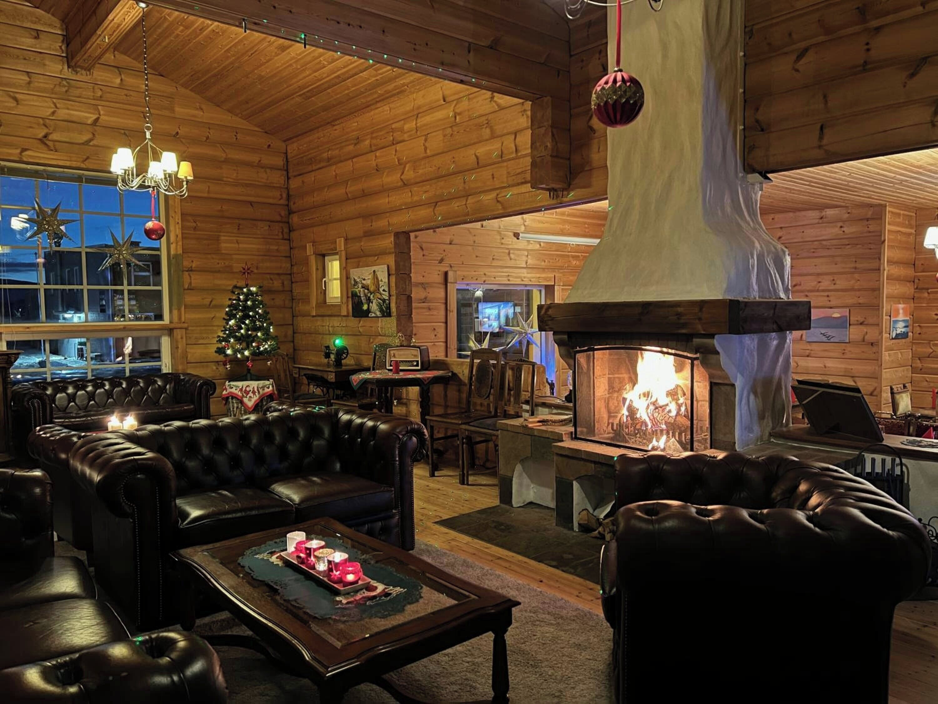 A cozy log cabin interior with a fireplace, leather furniture, and a Christmas tree.