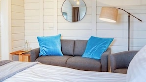A bedroom with a bed, a gray sofa with blue cushions, a round mirror, a ceiling fan, and a floor lamp. - Hotel Breiðdalsvík (Fjardabyggd)