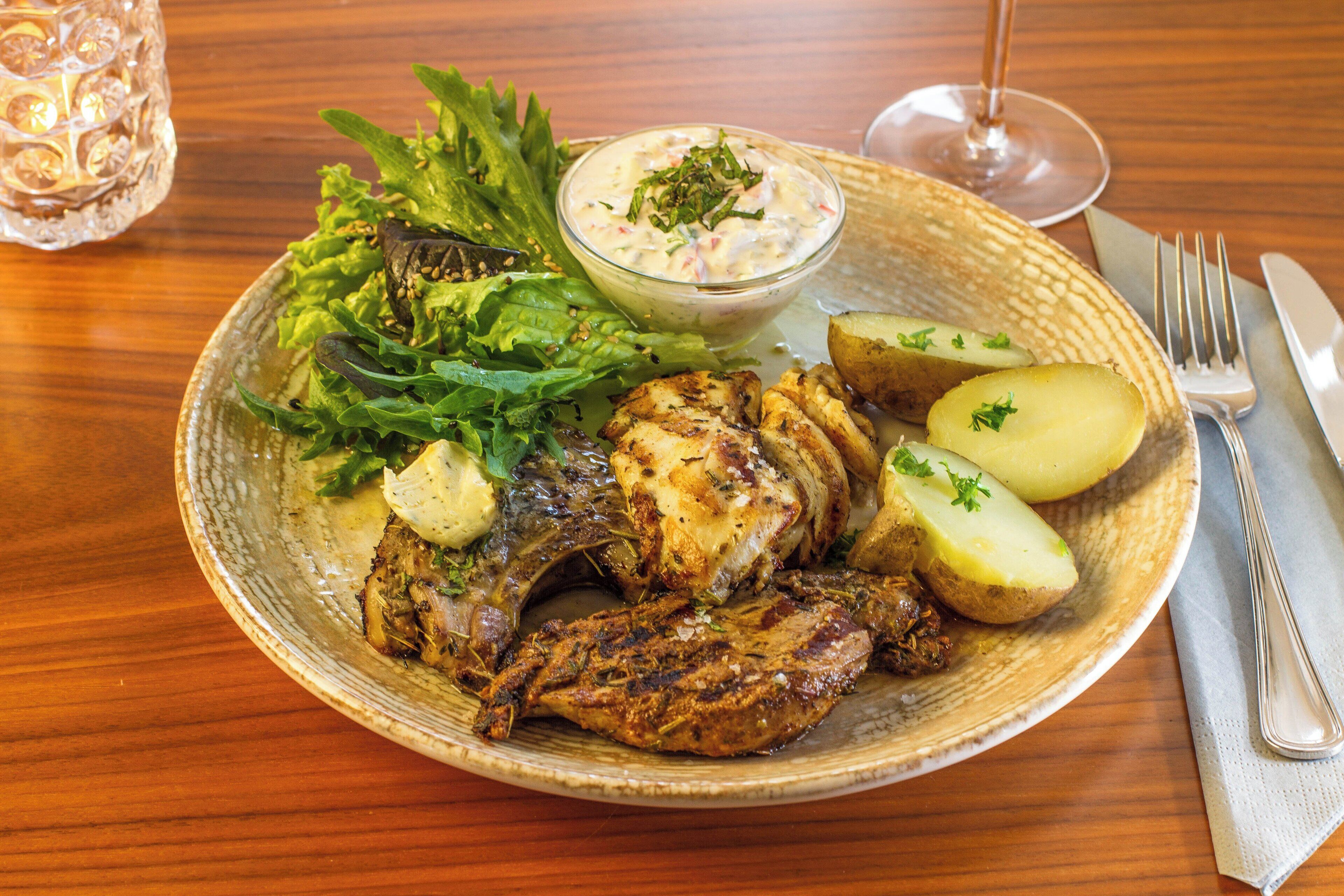 Un plato de comida que incluye pollo a la parrilla, papas y una ensalada con aderezo cremoso.