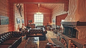 A cozy log cabin interior with leather sofas, a fireplace, and a large window. - Hotel Breiðdalsvík (Fjardabyggd)