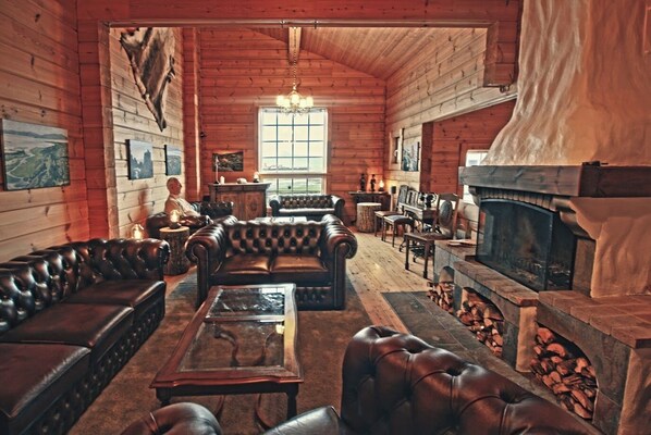 A cozy log cabin interior with leather sofas, a fireplace, and a large window. - Hotel Breiðdalsvík (Fjardabyggd)