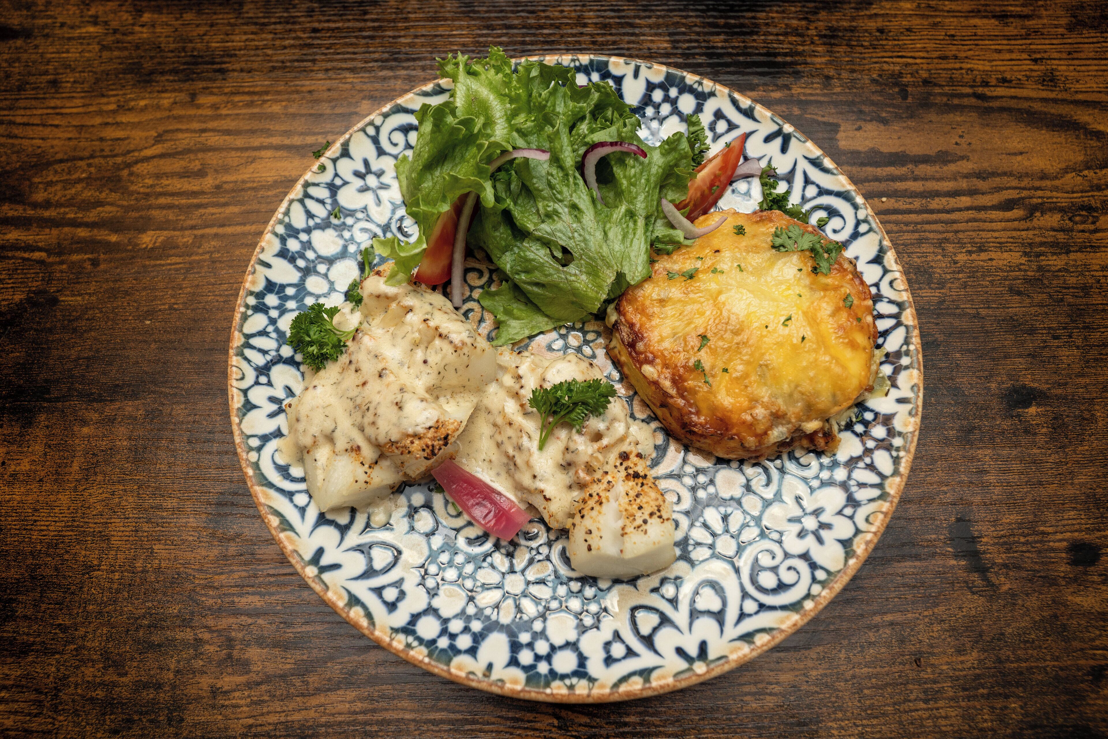 Une assiette contenant un morceau de poisson, une viennoiserie et une salade, le tout présenté sur une assiette à motifs.