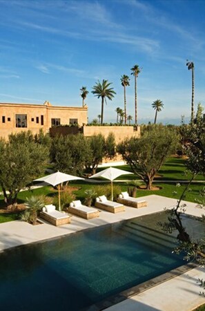 A pool area with lounge chairs and umbrellas, surrounded by palm trees and a building. - Les 5 Djellabas (Marrakech)