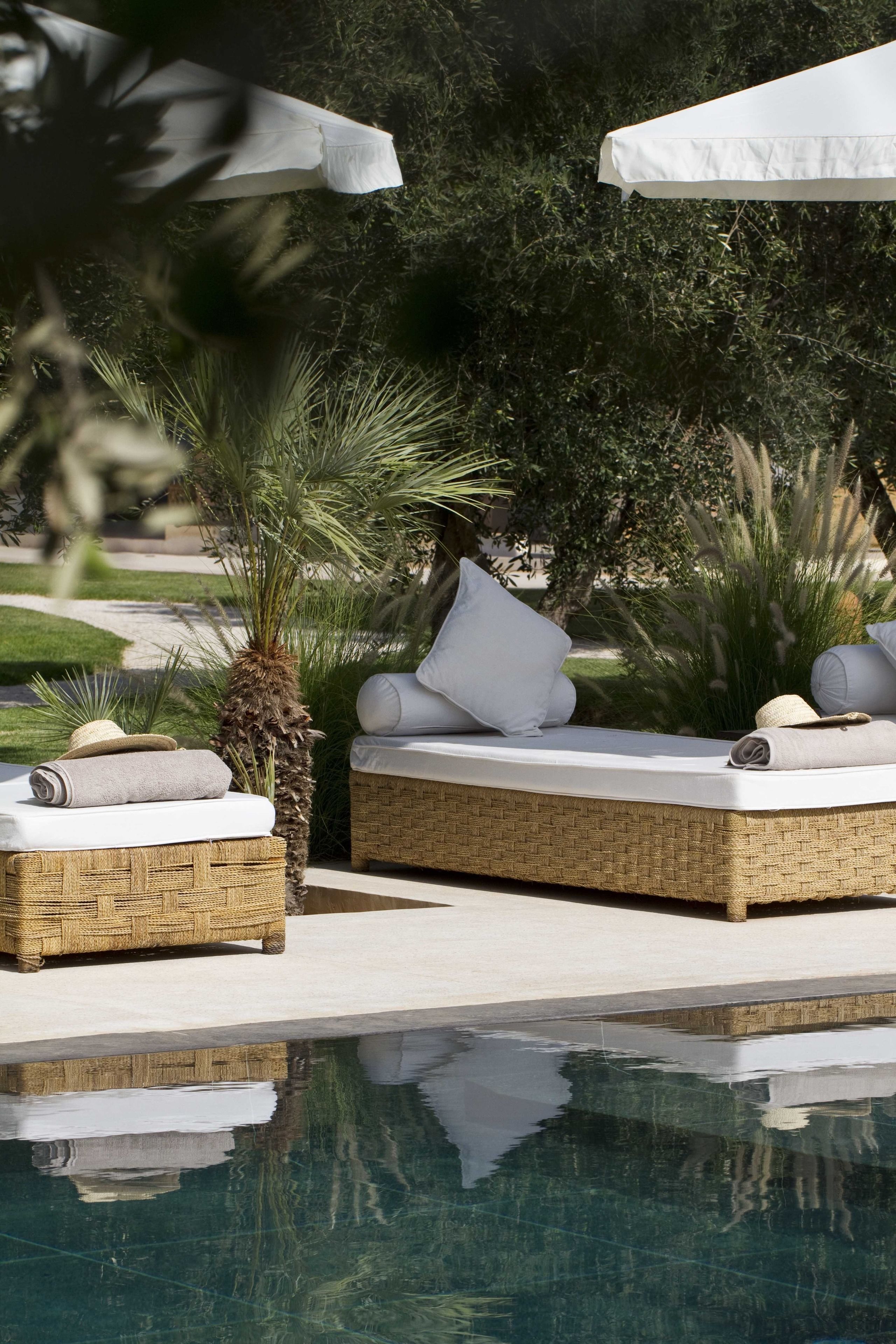 Un espace de détente aménagé au bord de la piscine, avec des meubles en osier, des coussins blancs et des parasols.