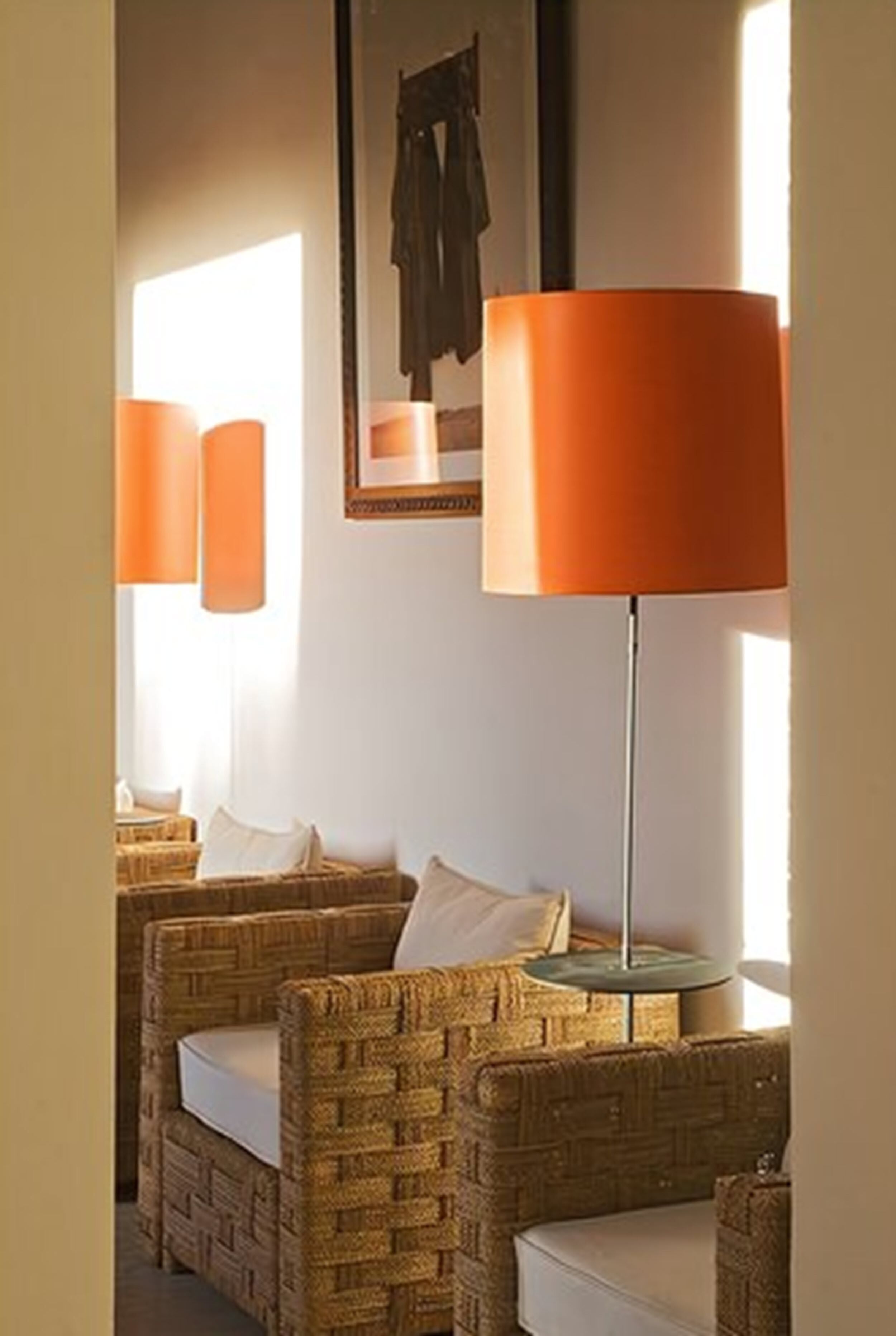 Sillas de mimbre con cojines blancos, una lámpara de pie y un cuadro en la pared.