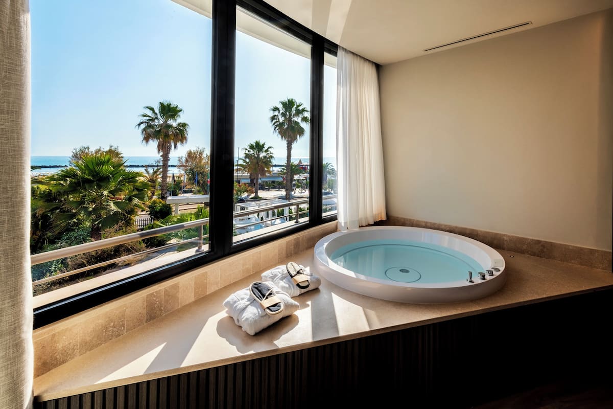 A modern bathroom with a large bathtub, a view of the sea, and a balcony with towels.