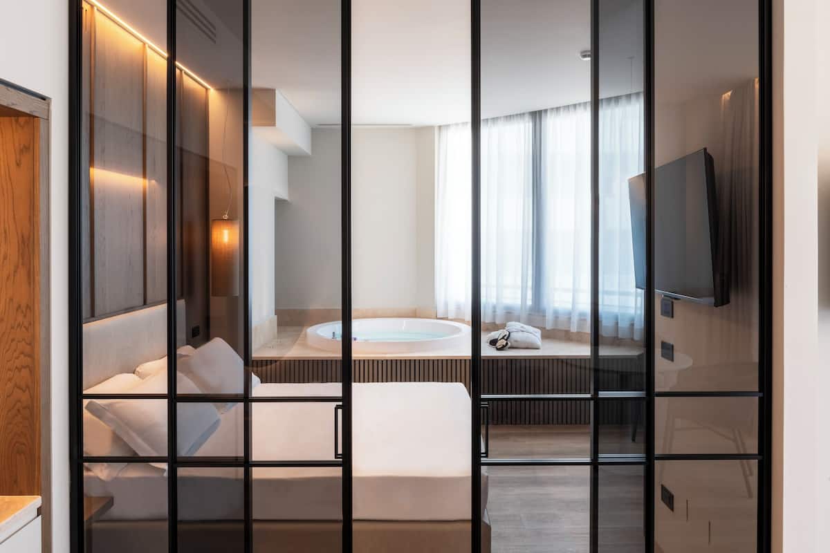 A modern hotel room with a large bed, a separate sitting area, a bathtub, and a television.