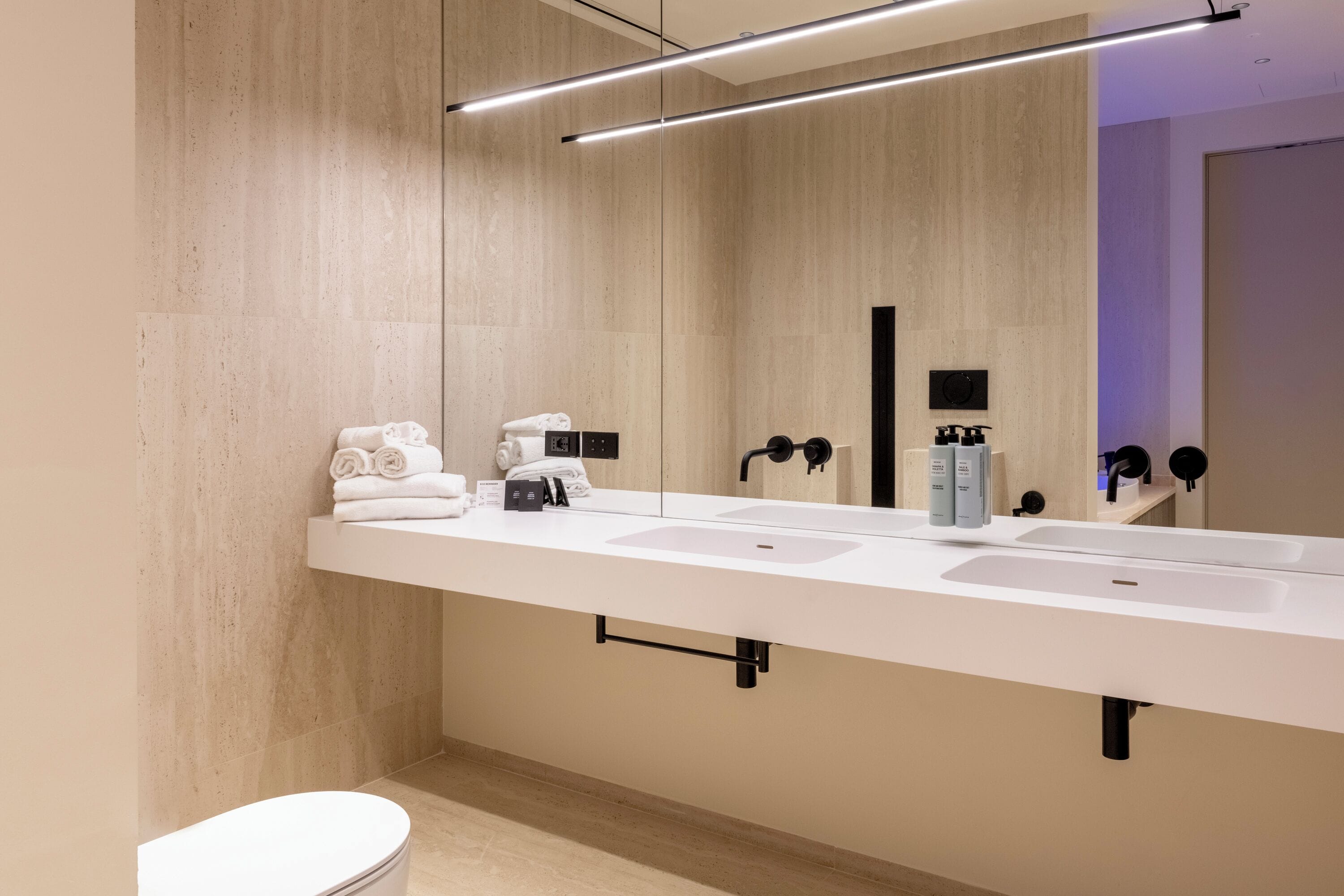 Un baño moderno con un lavamanos blanco alargado, un inodoro y un espejo grande.