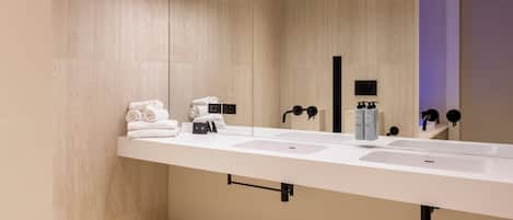 Un baño moderno con un lavamanos blanco alargado, un inodoro y un espejo grande.
