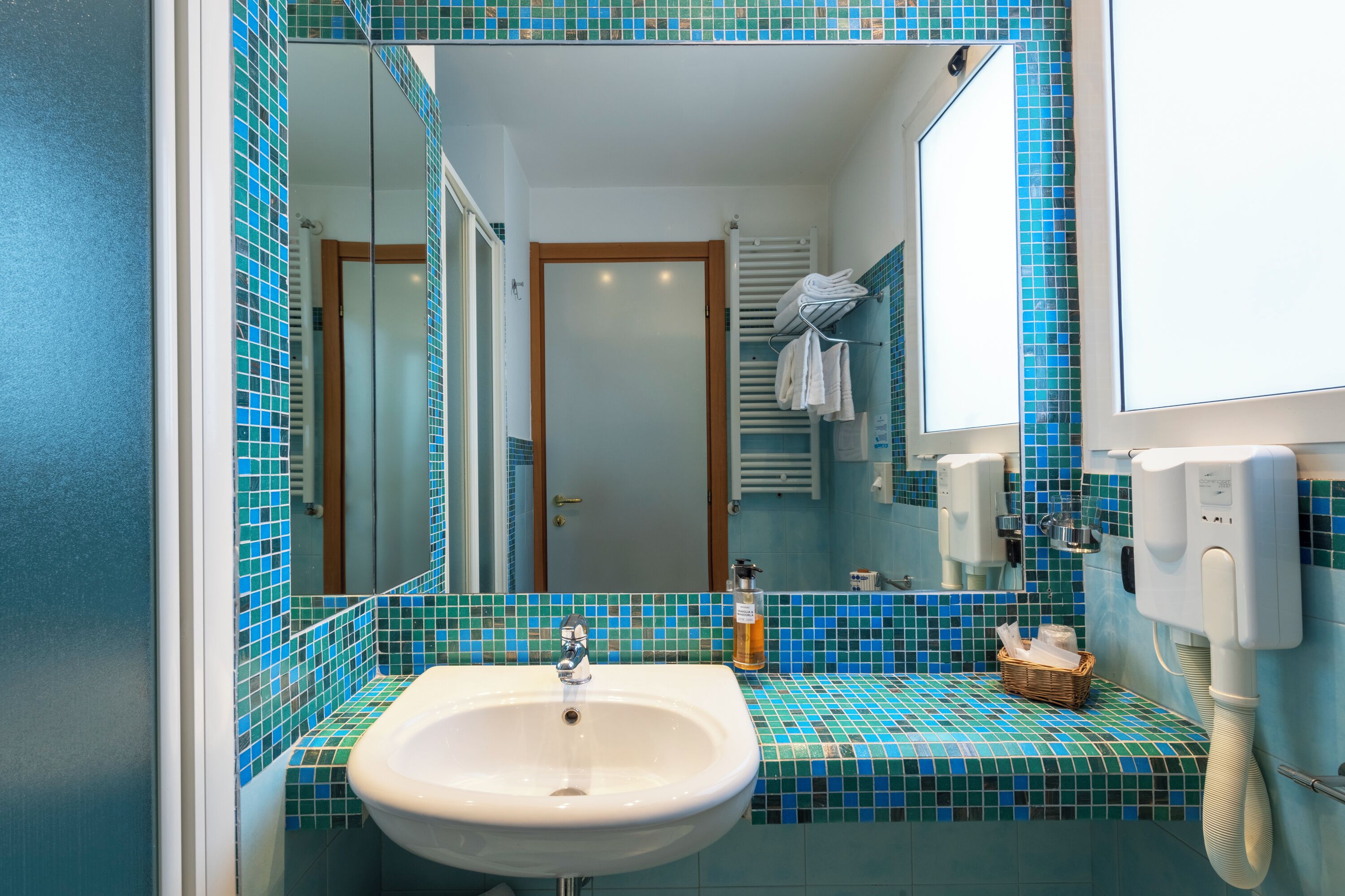 A bathroom with a white sink, blue-tiled walls, a mirror, a towel rack, and a hand dryer.