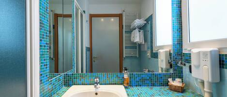 A bathroom with a white sink, blue-tiled walls, a mirror, a towel rack, and a hand dryer.